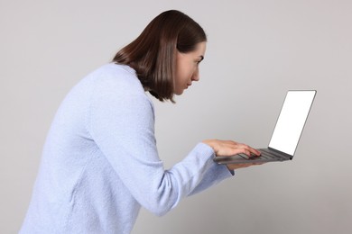 Woman with poor posture using laptop on gray background