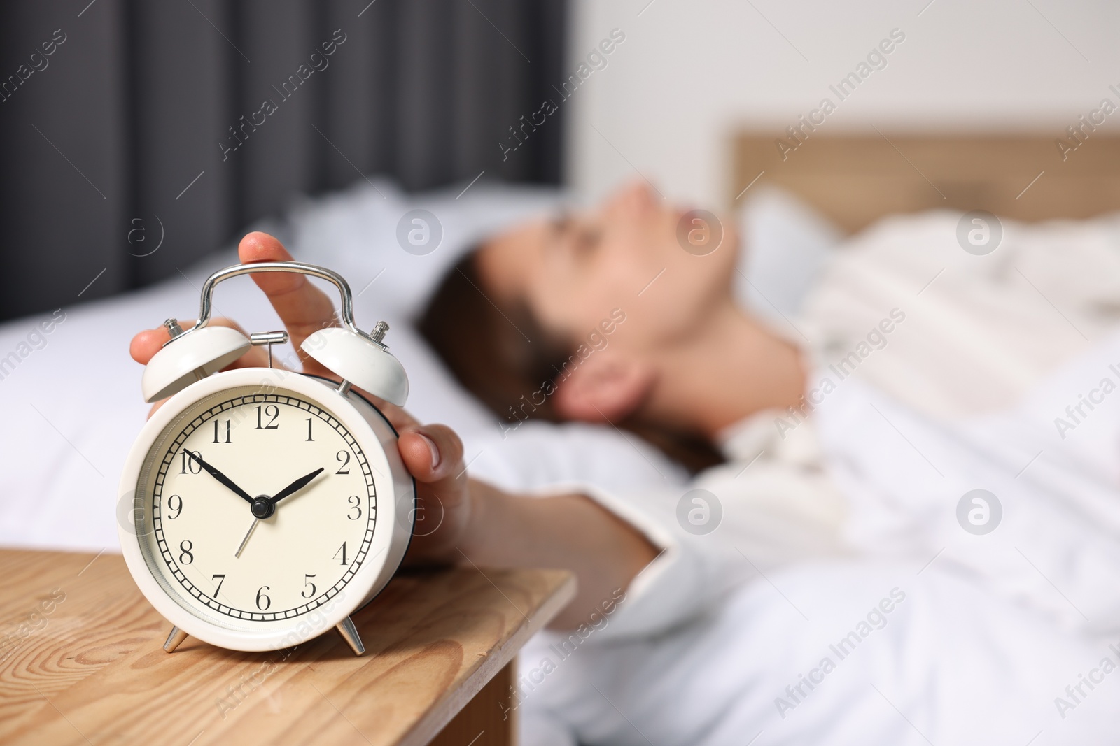 Photo of Woman turning off alarm clock in bedroom at lunch time, selective focus