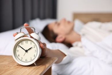 Woman turning off alarm clock in bedroom at lunch time, selective focus