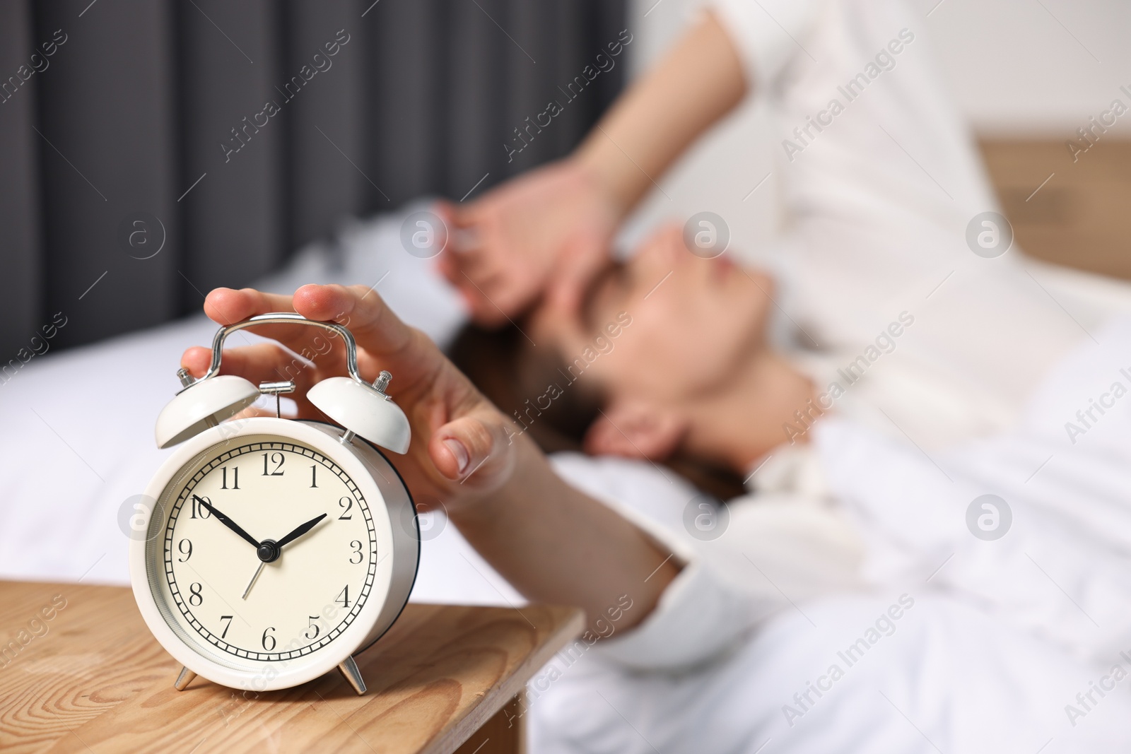 Photo of Woman turning off alarm clock in bedroom at lunch time, selective focus