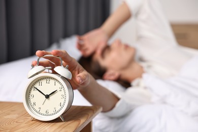 Woman turning off alarm clock in bedroom at lunch time, selective focus