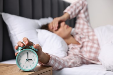 Woman turning off alarm clock in bedroom at lunch time, selective focus