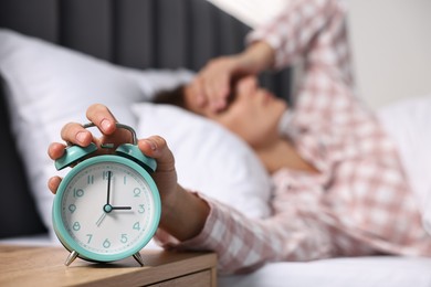 Woman turning off alarm clock in bedroom at lunch time, selective focus