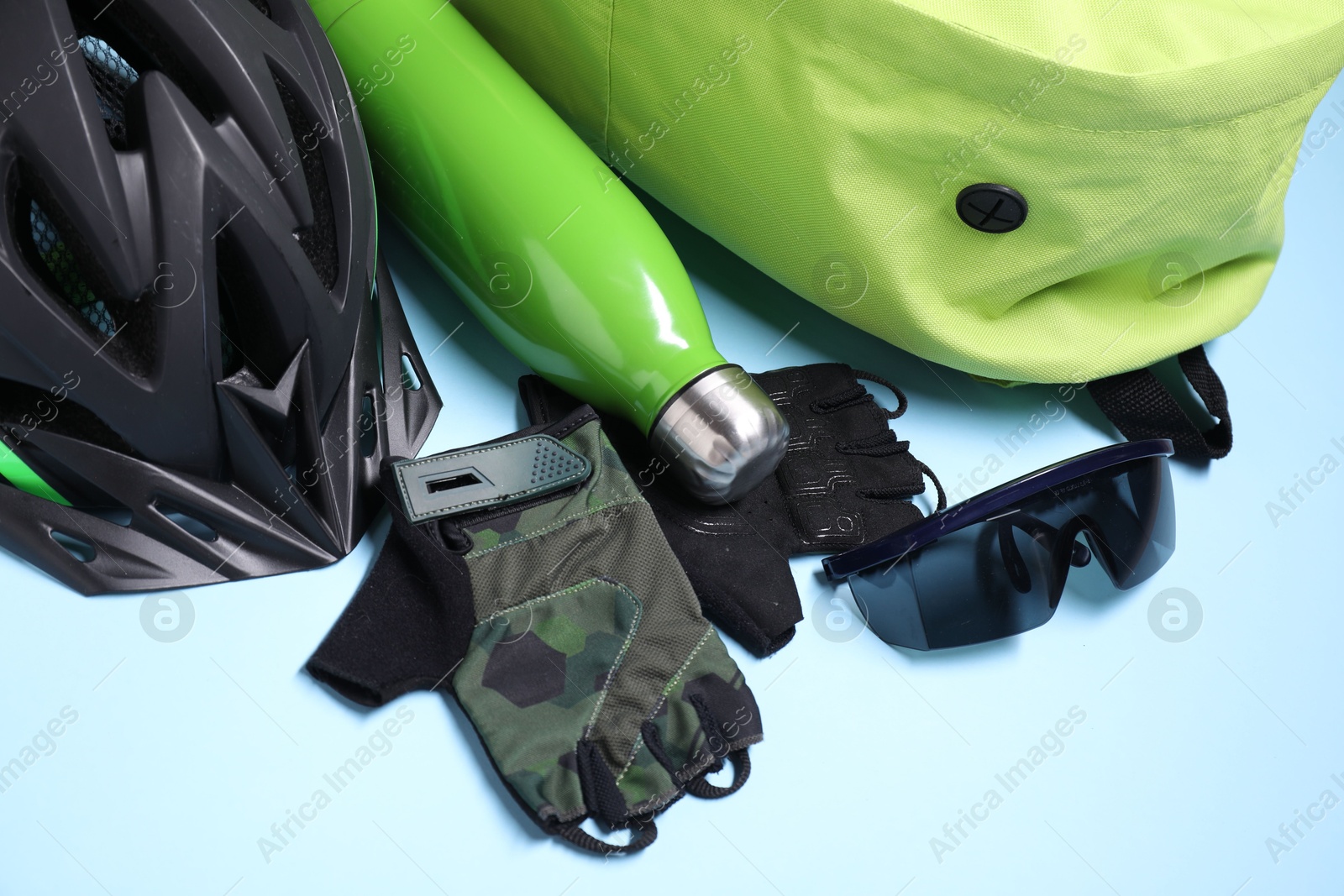 Photo of Bicycle helmet, thermo bottle, fingerless gloves and goggles on light blue background, closeup