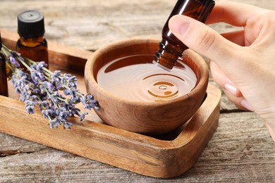 Photo of Woman dripping essential oil into bowl with water at wooden table, closeup