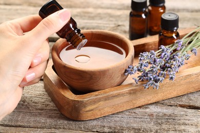 Photo of Woman dripping essential oil into bowl with water at wooden table, closeup