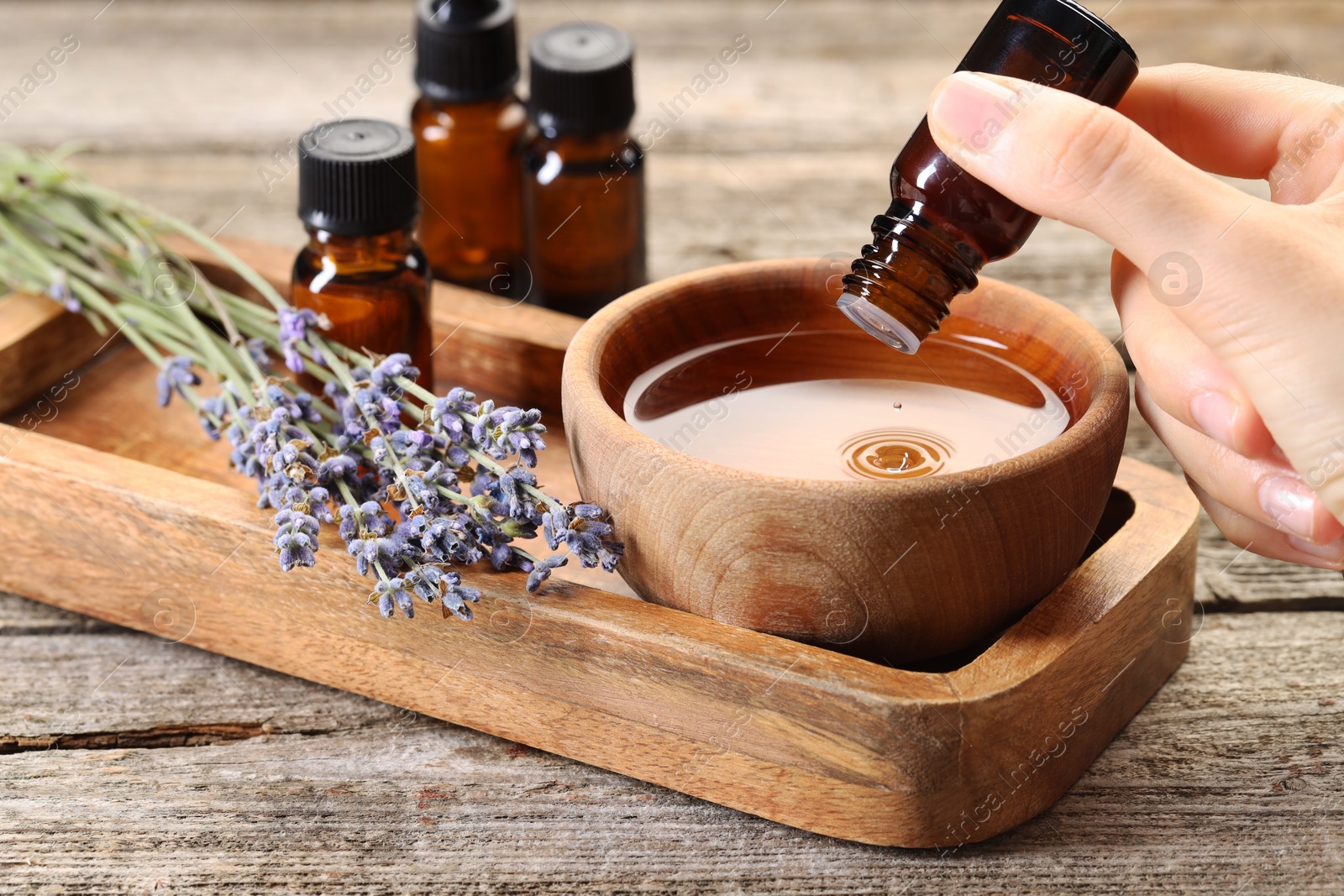 Photo of Woman dripping essential oil into bowl with water at wooden table, closeup