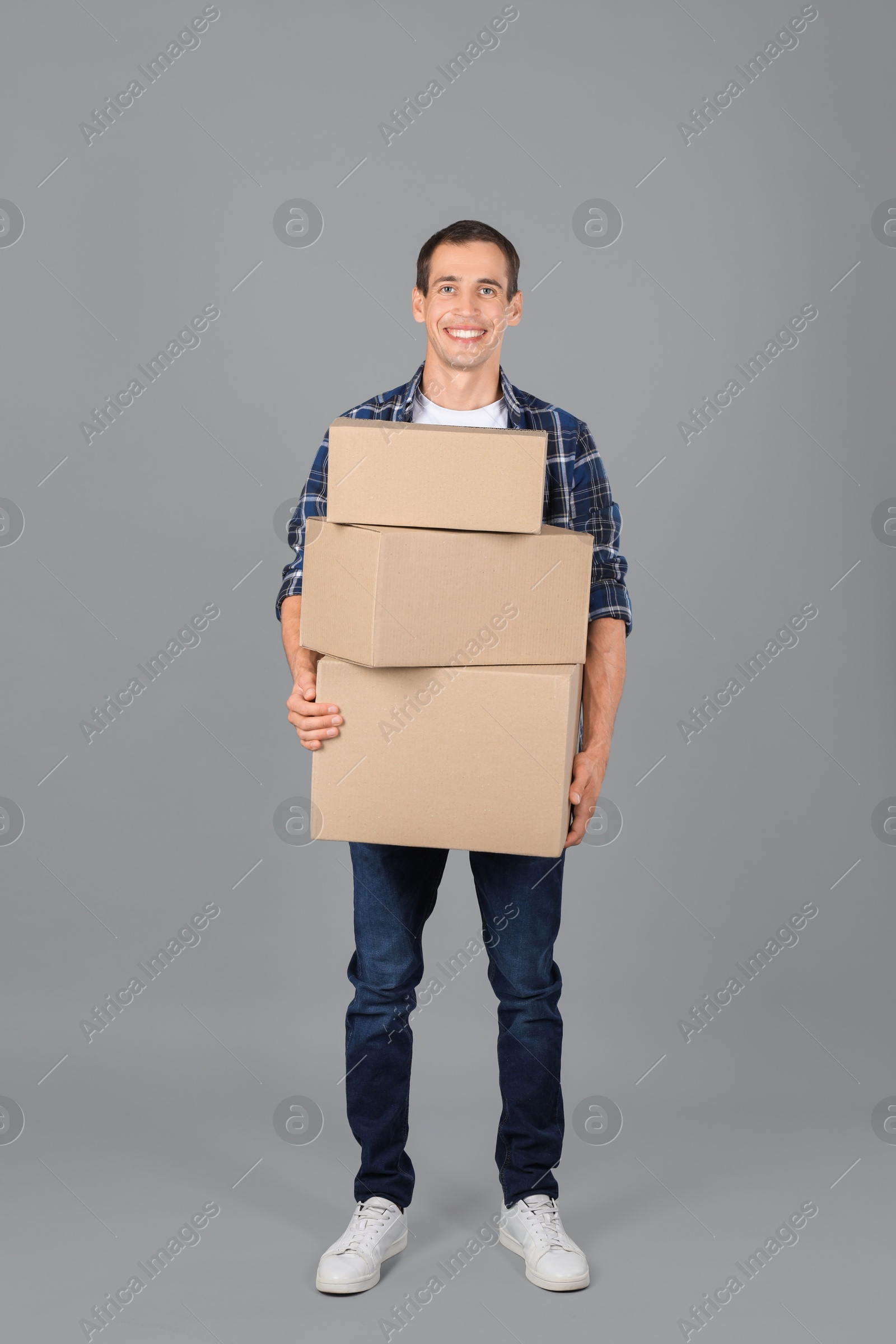 Photo of Moving into new house. Man with cardboard boxes on grey background