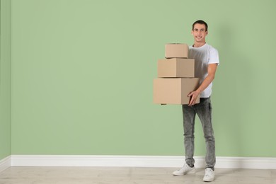 Photo of Moving into new house. Man with cardboard boxes near light green wall, space for text