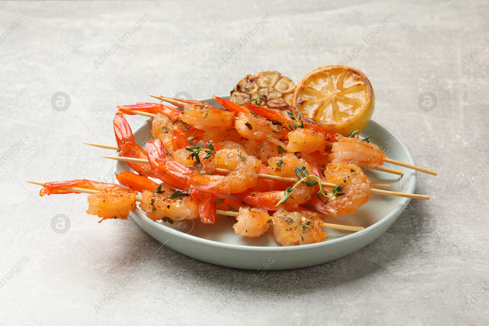 Photo of Delicious grilled shrimp skewers, lemon and garlic on light grey table