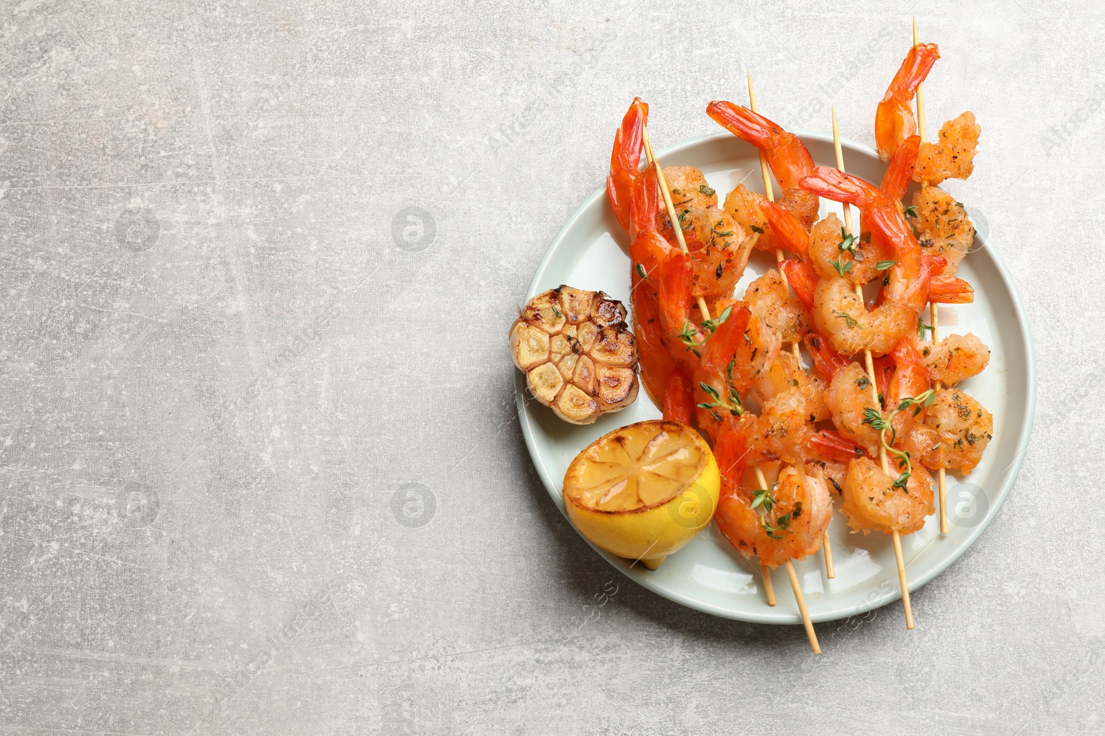 Photo of Delicious grilled shrimp skewers, lemon and garlic on light grey table, top view. Space for text