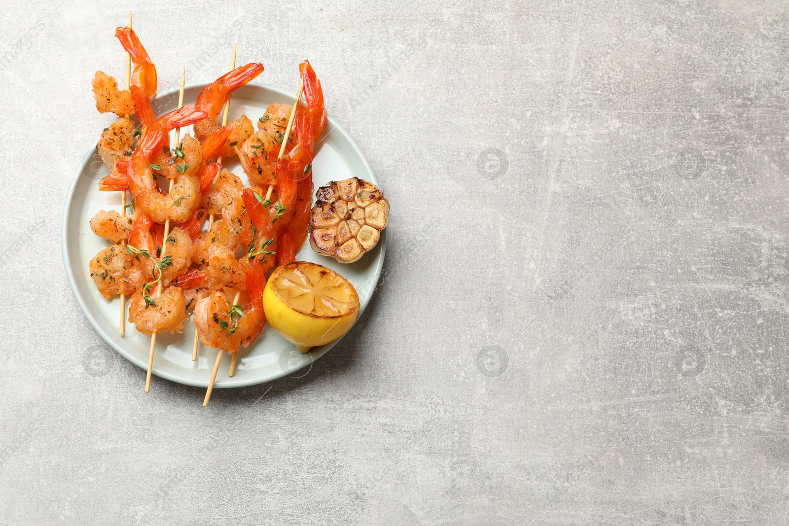 Photo of Delicious grilled shrimp skewers, lemon and garlic on light grey table, top view. Space for text