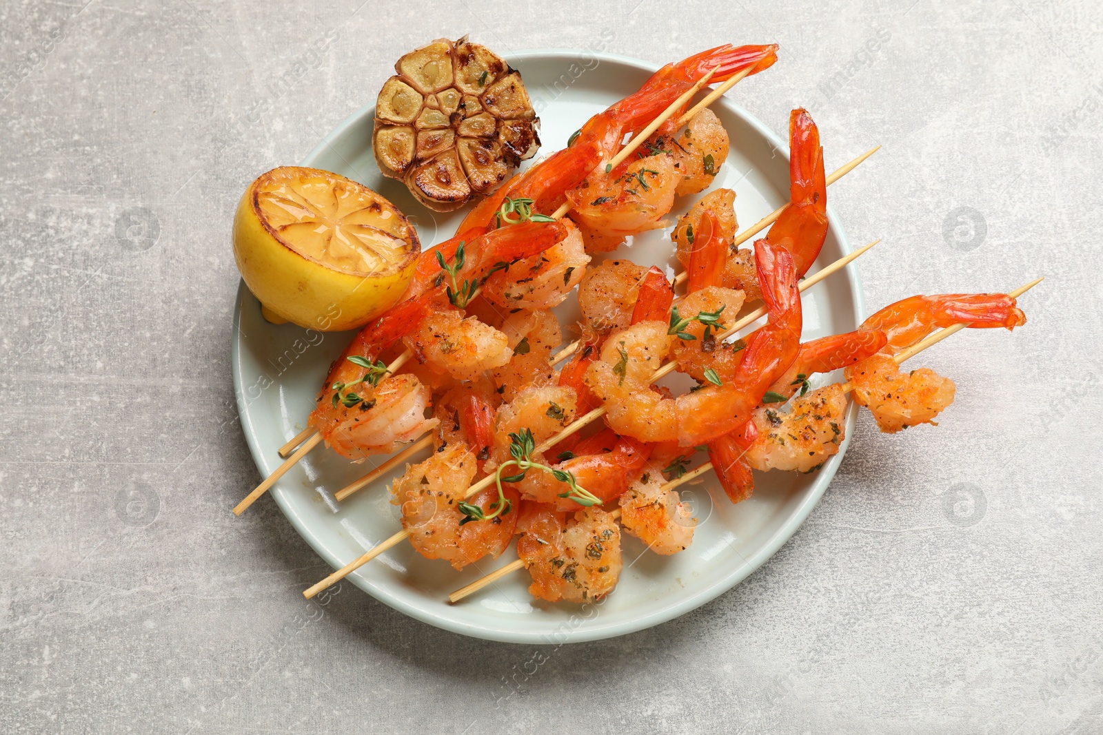 Photo of Delicious grilled shrimp skewers, lemon and garlic on light grey table, top view