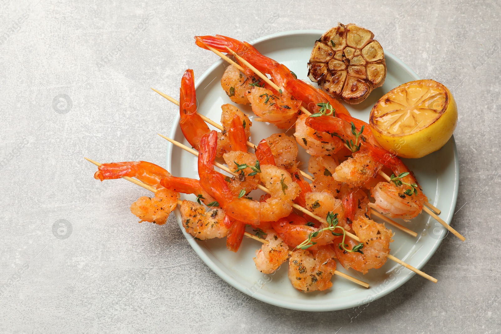 Photo of Delicious grilled shrimp skewers, lemon and garlic on light grey table, top view. Space for text