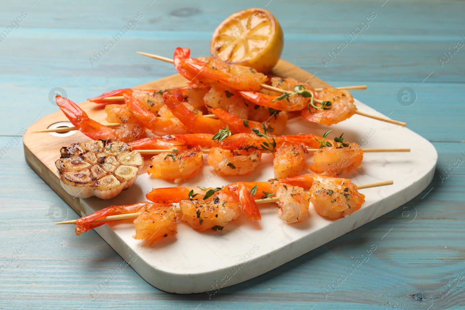 Photo of Delicious grilled shrimp skewers, lemon and garlic on light blue wooden table, closeup