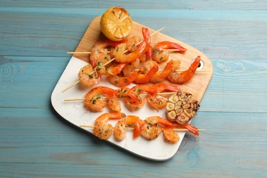 Photo of Delicious grilled shrimp skewers, lemon and garlic on light blue wooden table, top view