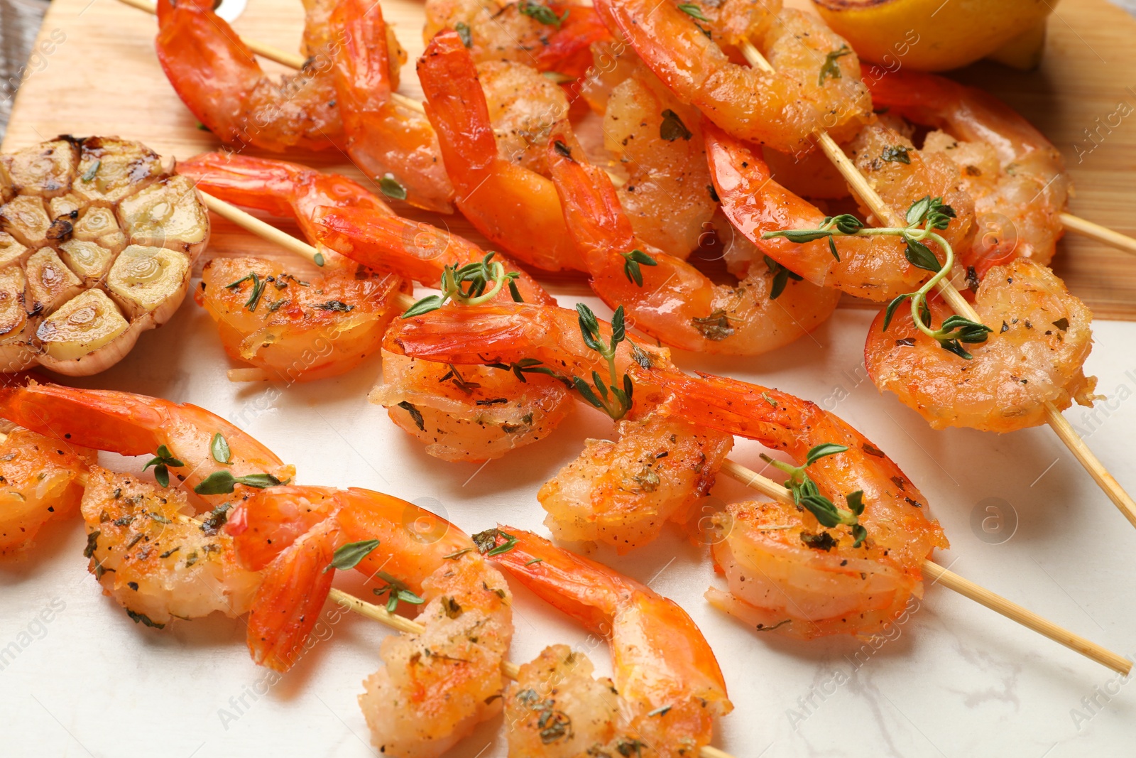 Photo of Delicious grilled shrimp skewers and garlic on board, closeup