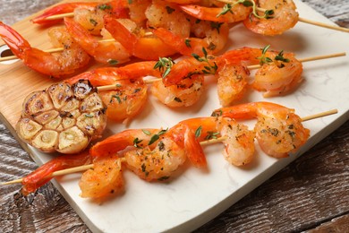 Photo of Delicious grilled shrimp skewers and garlic on wooden table, closeup