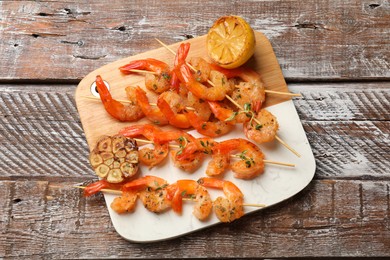 Photo of Delicious grilled shrimp skewers, lemon and garlic on wooden table, top view