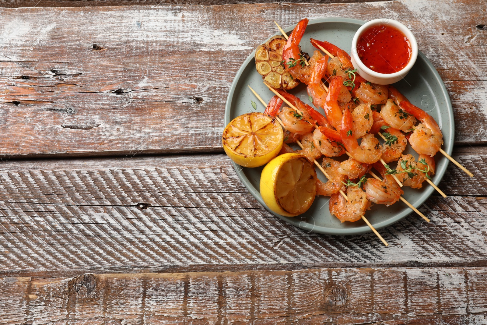 Photo of Delicious grilled shrimp skewers served with sauce and lemon on wooden table, top view. Space for text