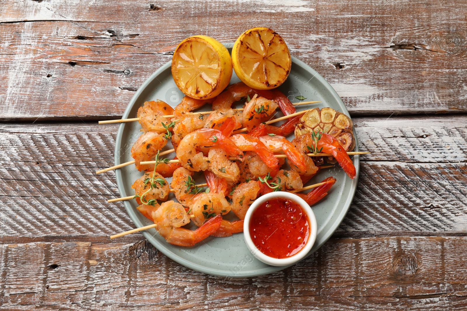 Photo of Delicious grilled shrimp skewers served with sauce and lemon on wooden table, top view