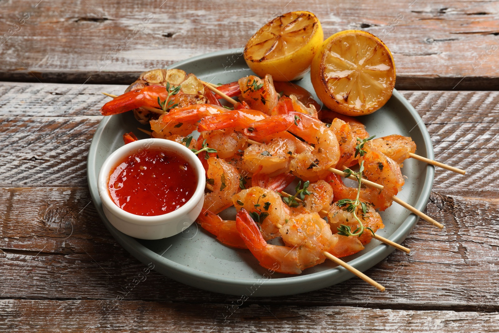 Photo of Delicious grilled shrimp skewers served with sauce and lemon on wooden table