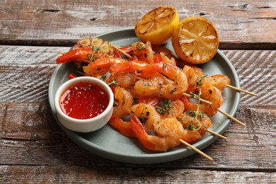 Photo of Delicious grilled shrimp skewers served with sauce and lemon on wooden table