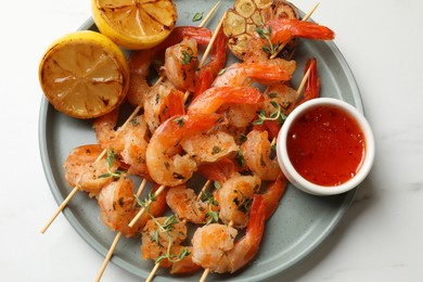 Photo of Delicious grilled shrimp skewers served with sauce and lemon on white marble table, top view