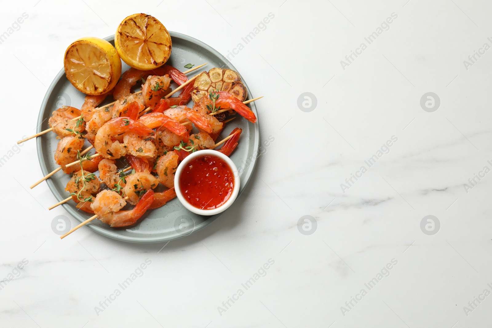 Photo of Delicious grilled shrimp skewers served with sauce and lemon on white marble table, top view. Space for text