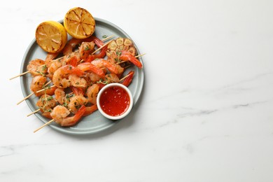 Photo of Delicious grilled shrimp skewers served with sauce and lemon on white marble table, top view. Space for text