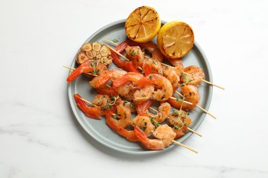 Photo of Skewers with delicious grilled shrimps, lemon and garlic on white marble table, top view