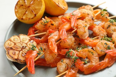 Photo of Delicious grilled shrimp skewers, garlic and lemon on white table, closeup