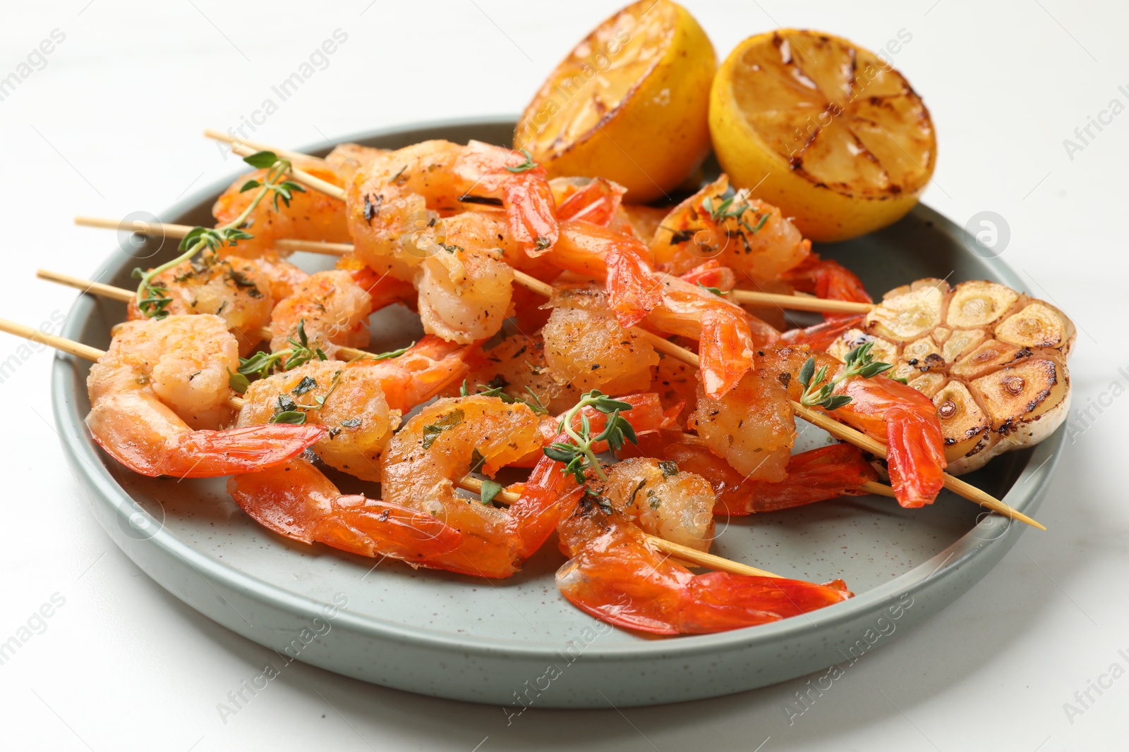 Photo of Delicious grilled shrimp skewers, lemon and garlic on white table, closeup