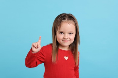 Portrait of cute little girl pointing at something on light blue background