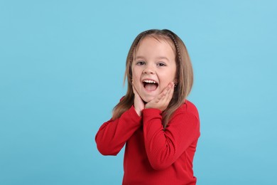 Portrait of emotional little girl on light blue background