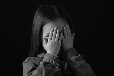 Photo of Girl covering face with hands on dark background, closeup. Black and white effect