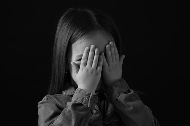 Girl covering face with hands on dark background, closeup. Black and white effect