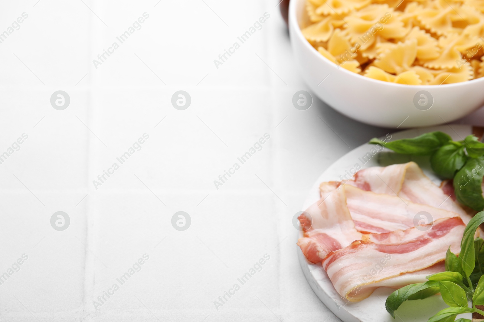 Photo of Raw pasta and fresh ingredients on white tiled table, space for text