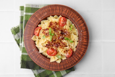 Tasty pasta with bacon, tomatoes and basil on white tiled table, top view