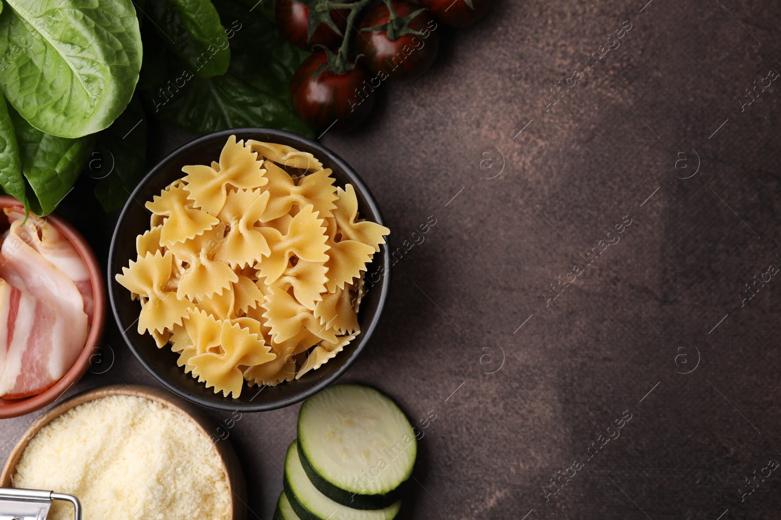 Photo of Raw pasta, bacon and fresh ingredients on brown table, flat lay