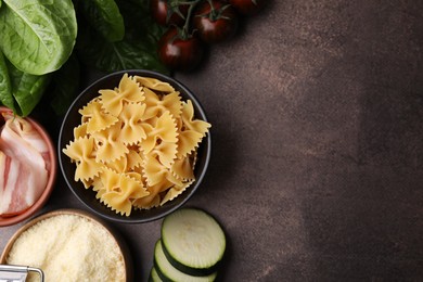 Photo of Raw pasta, bacon and fresh ingredients on brown table, flat lay