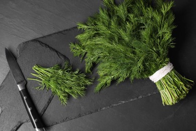 Photo of Sprigs of fresh green dill and knife on black table, top view