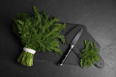 Photo of Sprigs of fresh green dill and knife on black table, top view