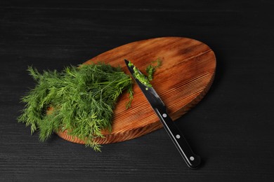 Photo of Sprigs of fresh green dill and knife on black wooden table