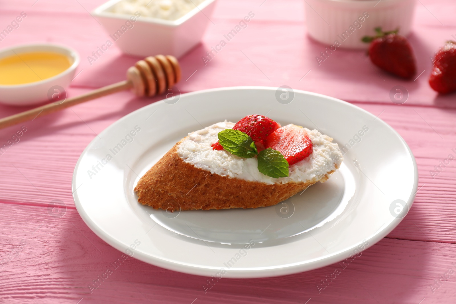 Photo of Delicious ricotta bruschetta with strawberry and mint on pink wooden table