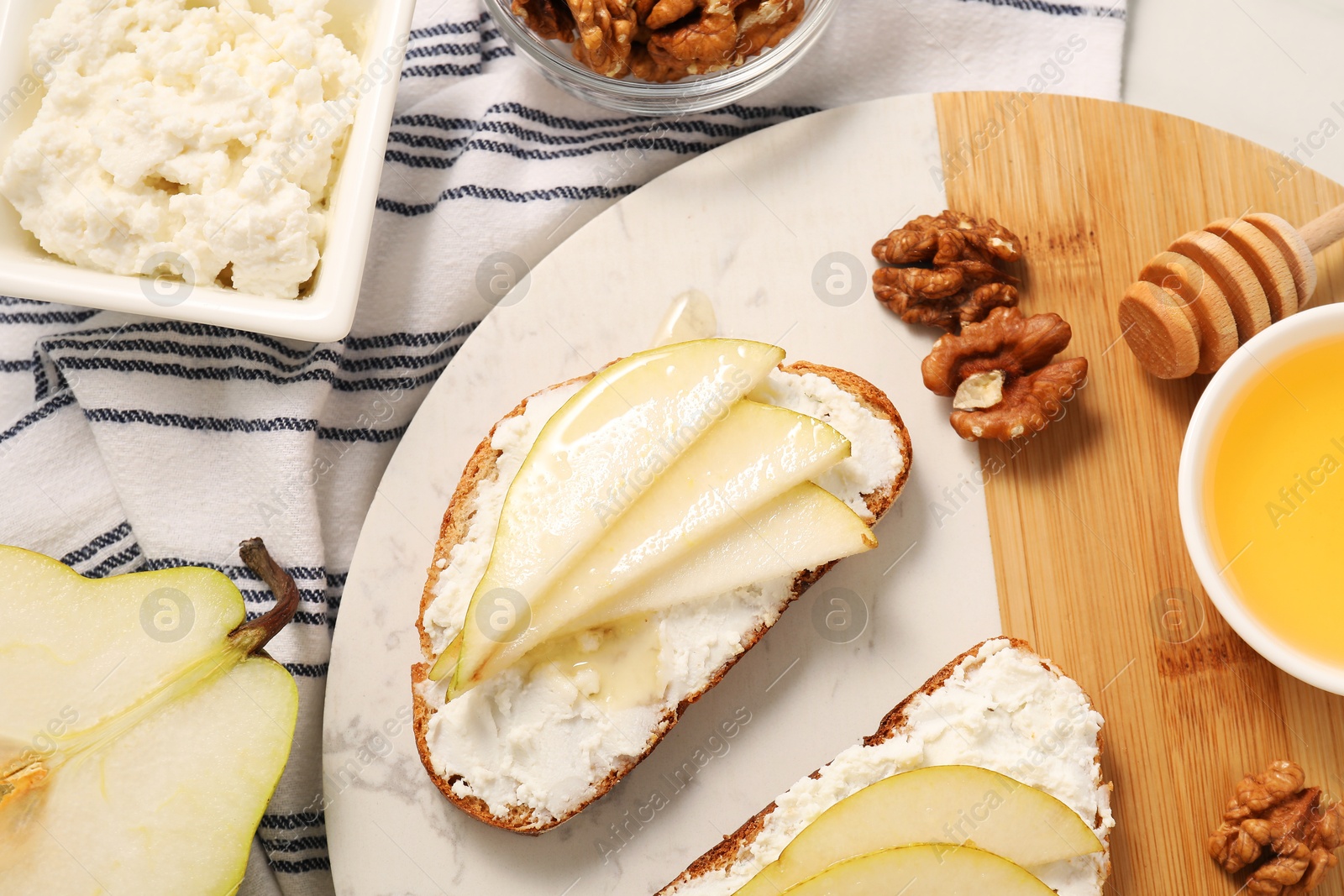 Photo of Delicious ricotta bruschettas with pear and walnut on white table, flat lay