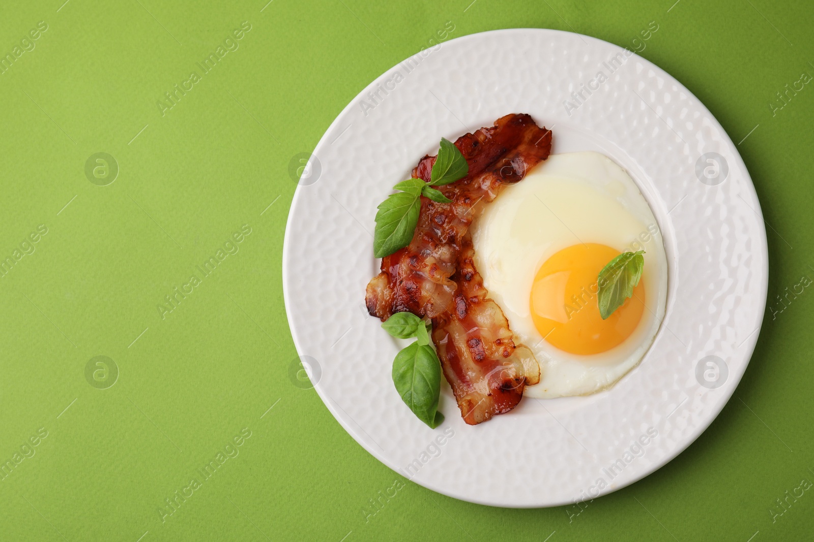 Photo of Fried egg, bacon and basil on green background, top view. Space for text