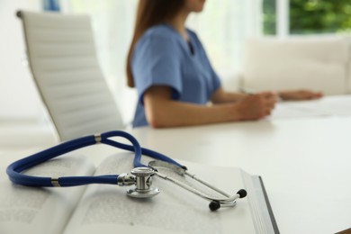 Photo of Doctor at white table in hospital, focus on medical stethoscope and book