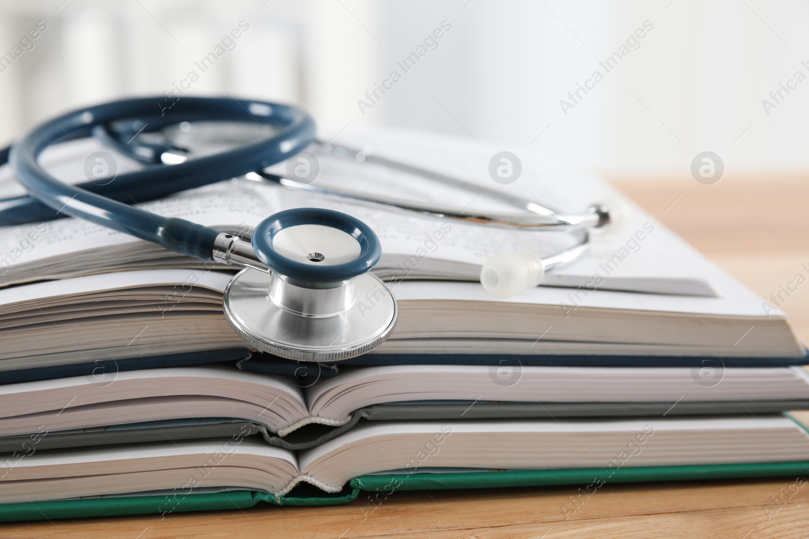 Photo of One new medical stethoscope and books on wooden table, closeup