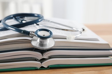 Photo of One new medical stethoscope and books on wooden table, closeup